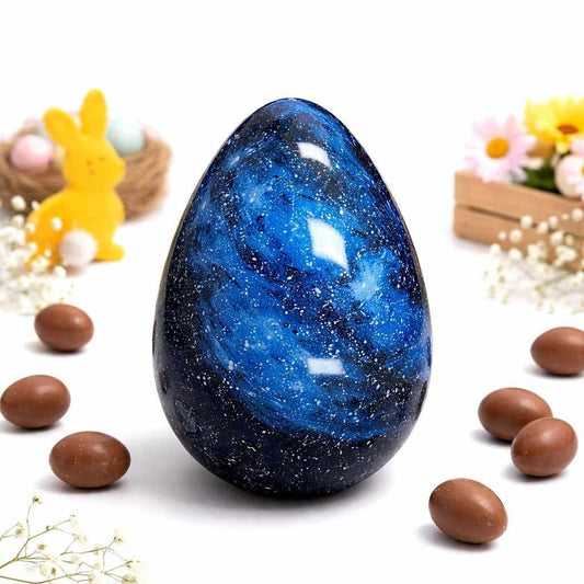Blue speckled egg-shaped object on a white surface with chocolate eggs and decorative items.
