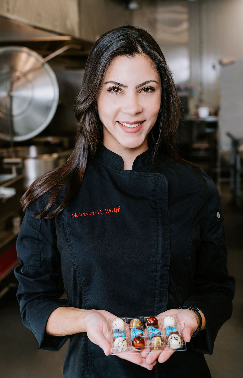 Marina Wolff smiling while holding with her 2 hands a tray with colourful bonbons 